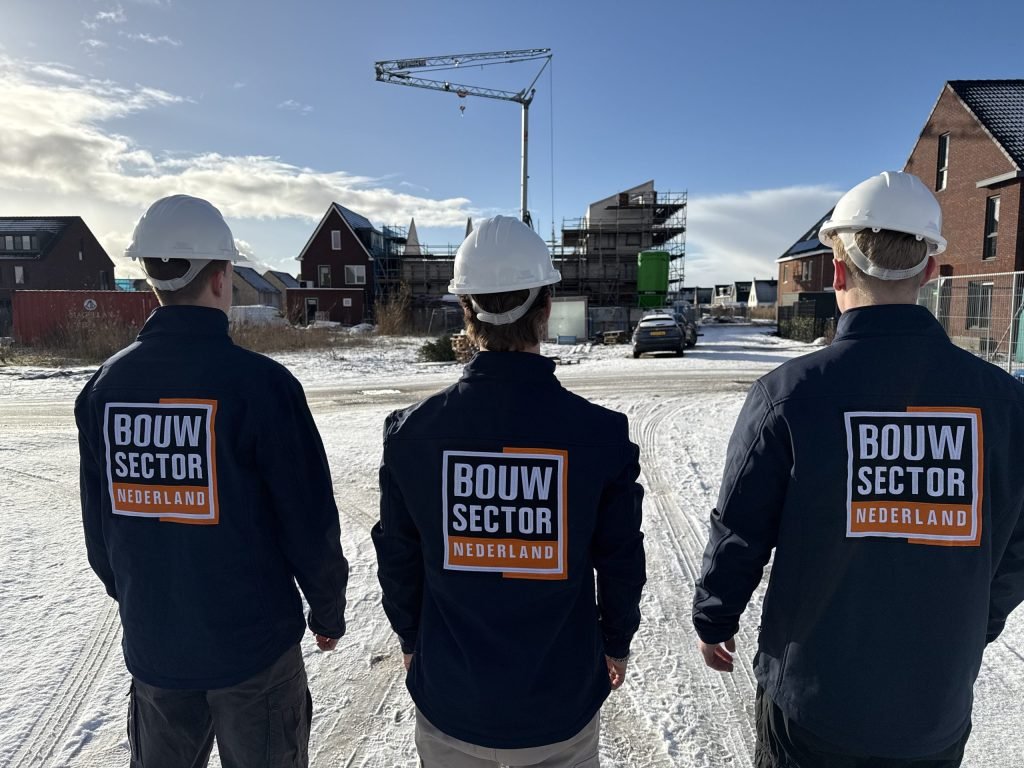 Drie collega's van Bouwsector Nederland met witte helm en werkjas kijken naar woningen in aanbouw in de sneeuw